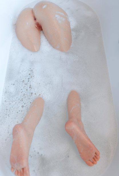 Realistic silicone female body part with detailed anatomy floating in soapy bath water, showcasing lifelike skin texture and natural curves.