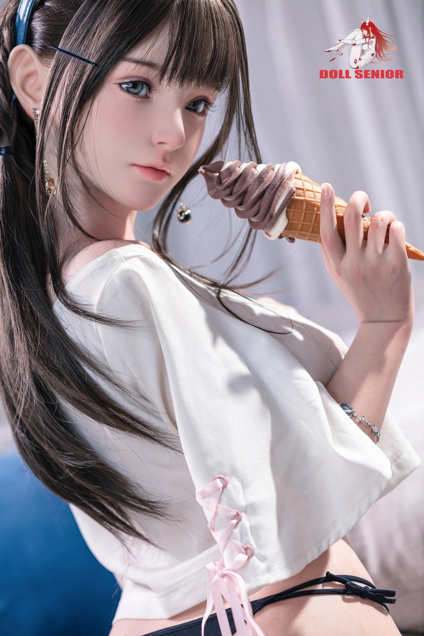 Realistic female doll with brown hair, green eyes, holding chocolate ice cream cone, wearing white top with pink laces