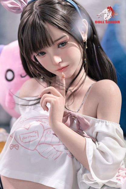 Realistic female doll with brown hair, green eyes, wearing white top with pink bow and bunny ears, soft skin texture