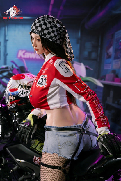 Realistic female doll in red racing jacket, checkered bandana, denim shorts, and fishnet stockings, posed on motorcycle.
