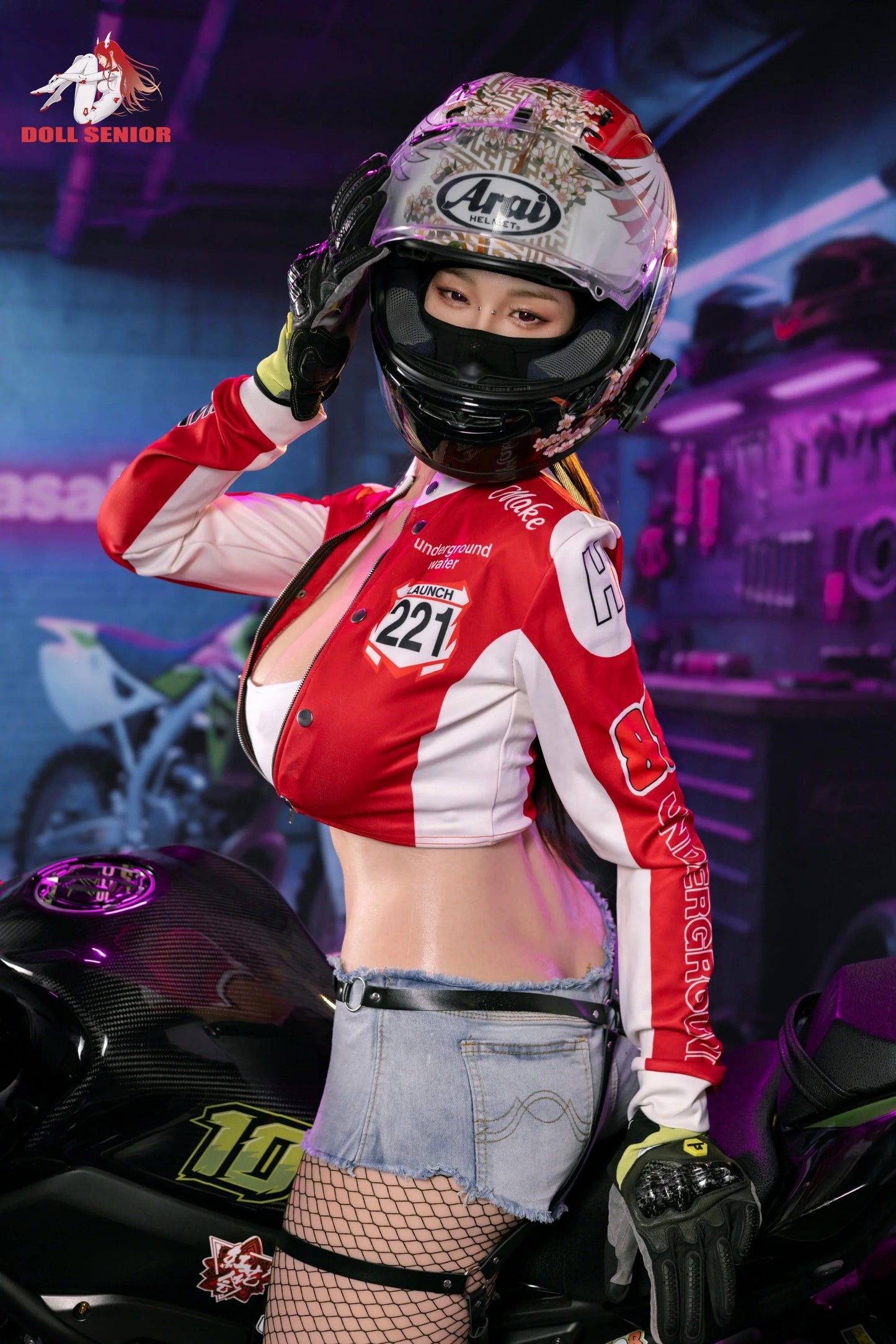 Realistic female doll in red racing jacket, floral helmet, denim shorts, and fishnet stockings beside motorcycle