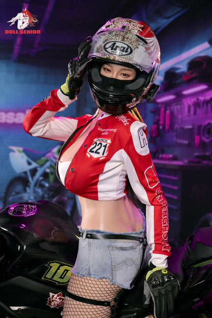Realistic female doll in red racing jacket, floral helmet, denim shorts, and fishnet stockings beside motorcycle