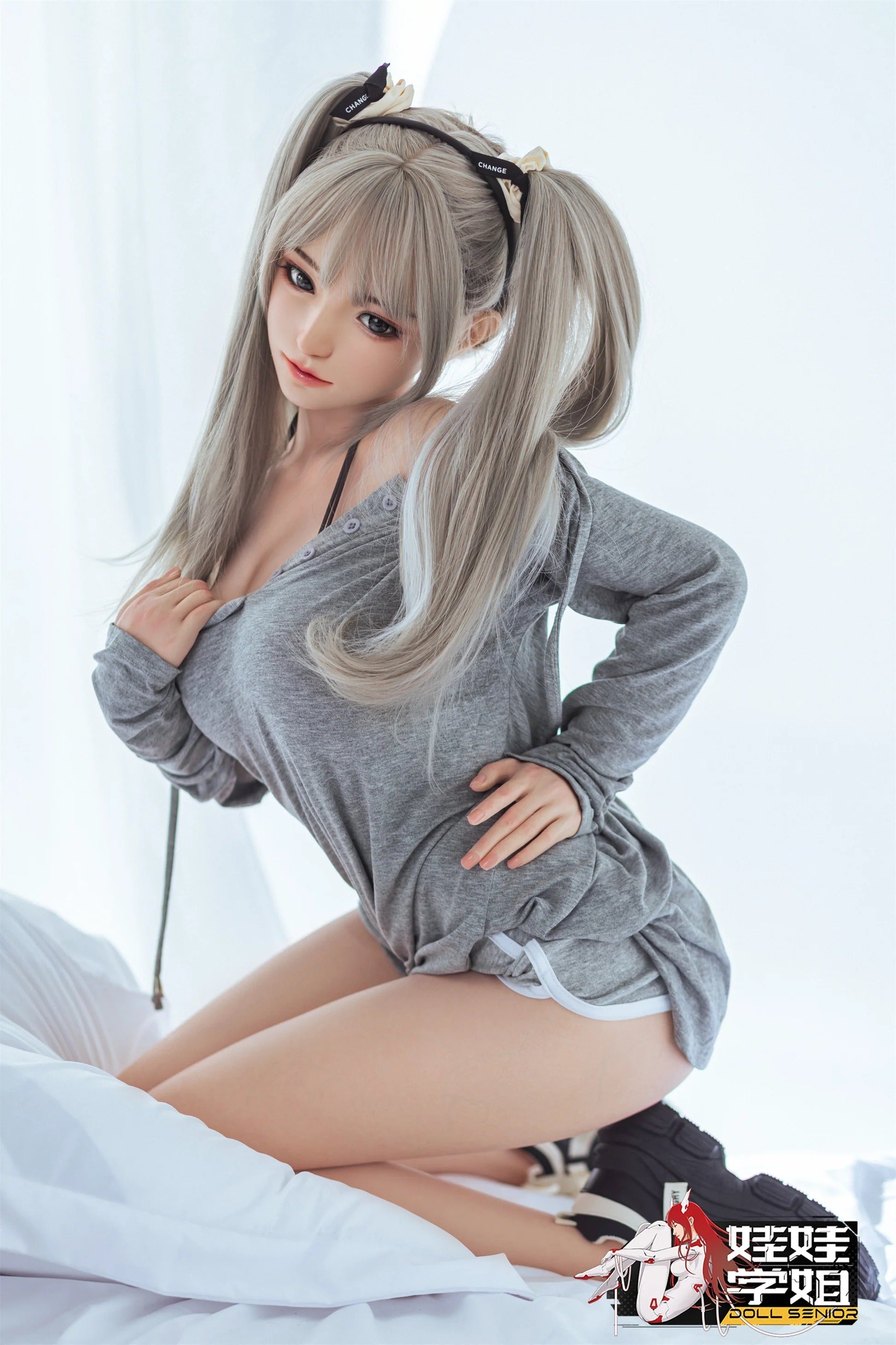 Realistic female doll with silver pigtails, gray top, and lifelike skin texture posing on white bedding